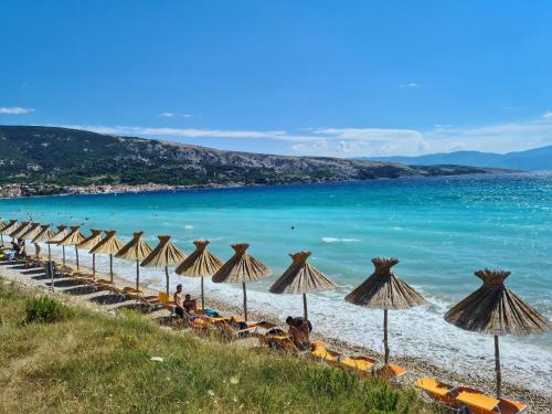 a row of umbrellas on a beach with the ocean at Ferienhaus mit Meerblick & Pool in Baška - Villa-Planina in Baška