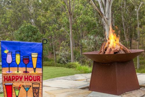 a fire pit and a sign with a happy hour sign at Stylish rural retreat on the foothills of Mt. Mee in Upper Caboolture