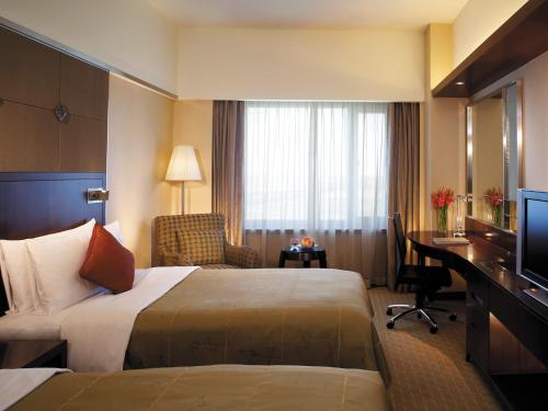a hotel room with two beds and a desk and a television at Shangri-La Harbin in Harbin