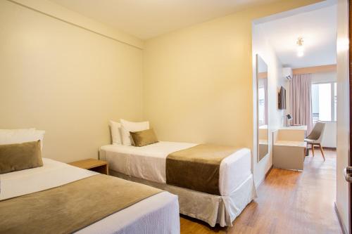 a hotel room with two beds and a desk at Jandaia Turismo Hotel in Santana do Livramento
