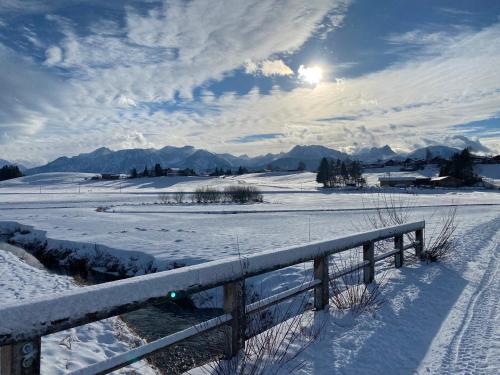a fence in a snow covered field with the sun at Ferienwohnung Allgäuer Landhaus Stocker in Hopferau-Füssen in Hopferau