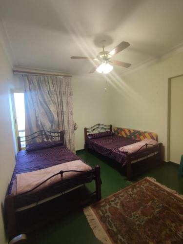 two beds in a room with a ceiling fan at شقة ايفو ترى المنتزه بالكامل in Alexandria