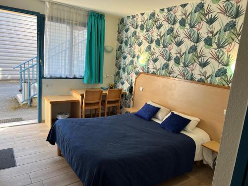 een slaapkamer met een bed met blauwe lakens en een tafel bij Hôtel Le Laury's in Onet le Château