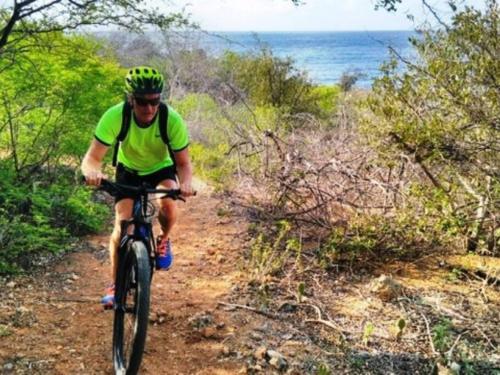 Um homem a andar de bicicleta num trilho de terra perto do oceano. em Local Willibrord Lodge em Willibrordus