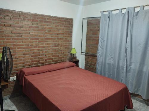 1 dormitorio con cama roja y pared de ladrillo en Dpto. 1 Lopez, de Ariel Reynoso en Mina Clavero