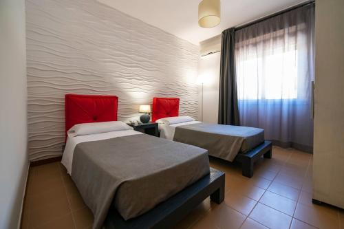 two beds in a hotel room with red pillows at Aparthotel Isabella in Sciacca