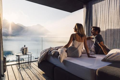 Ein Mann und eine Frau sitzen auf einem Bett in einem Schlafzimmer in der Unterkunft Seehotel Einwaller - adults only in Pertisau