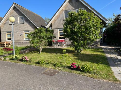 a house with a tree and flowers in the yard at Perle am Ijsselmeer mit eigenem Tretboot in Medemblik