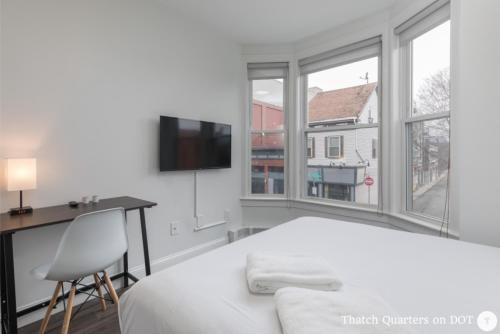 a white bedroom with a bed and a desk and windows at Quarters on DOT by Thatch in Boston