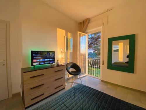 una camera da letto con cassettiera, TV e finestra di Villa Boeddu, relax tra mare e campagna ad Alghero