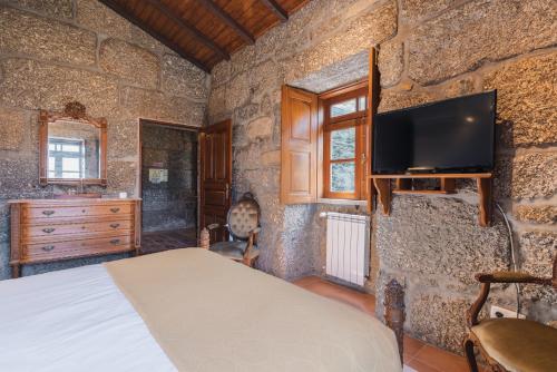 a bedroom with a bed and a tv on a stone wall at Quinta do Outeiro in Resende
