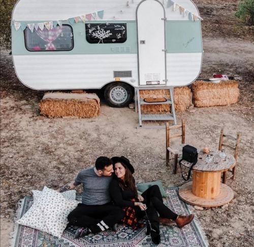 a couple sitting on a rug in front of a trailer at SA MOLA GLAMPING EXPERIENCE Roulotte in Escolca