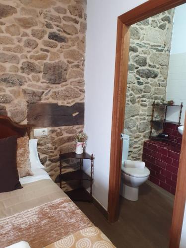 a bedroom with a stone wall and a bed and a toilet at La Pallota de San Cristobal in Palas de Rei