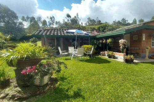 a yard with chairs and an umbrella and a house at Acogedora casa de campo en el oriente de Antioquia in El Retiro