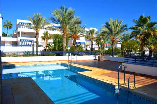 a swimming pool with palm trees and a building at Apartamento Pueblo Dorado in Mojácar