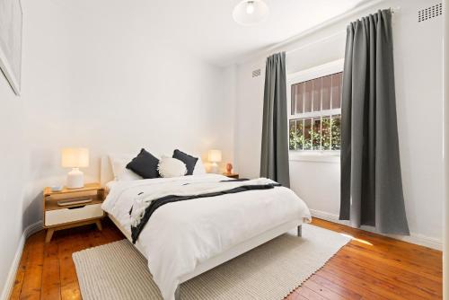 a white bedroom with a bed and a window at Beach-side North Bondi in Sydney