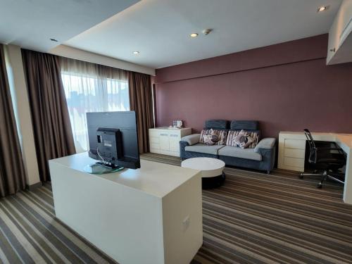een woonkamer met een bank en een bureau met een televisie bij Hotel Capital Kota Kinabalu in Kota Kinabalu