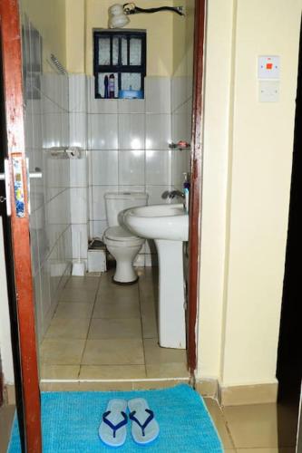 a bathroom with a sink and a toilet and a pair of slippers at EuphGlory Accomodations in Kakamega