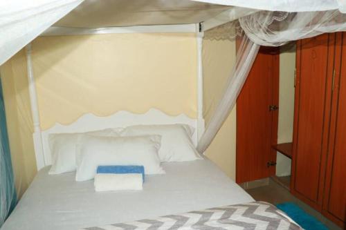 EuphGlory Accomodations في Kakamega: غرفة نوم مع سرير المظلة مع الوسائد البيضاء