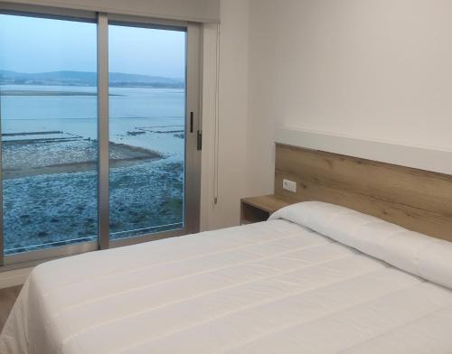 a bedroom with a white bed and a large window at Apartamentos O Grove Awa Bay in O Grove