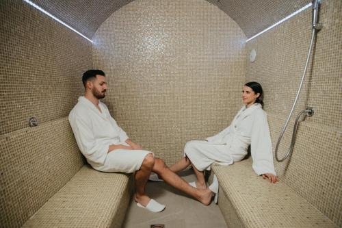 Un uomo e una donna seduti su panchine in una doccia di Artist hotel a Subotica