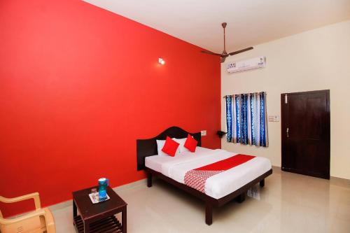 Dormitorio con paredes rojas, cama y mesa en Hotel Aljemin en Kanyakumari
