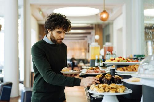 a man standing at a buffet with plates of food at Sheraton Diana Majestic in Milan