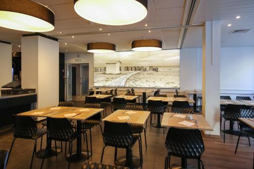 een restaurant met houten tafels en stoelen en een muurschildering bij Hotel Sandeshoved Zeedijk in Nieuwpoort
