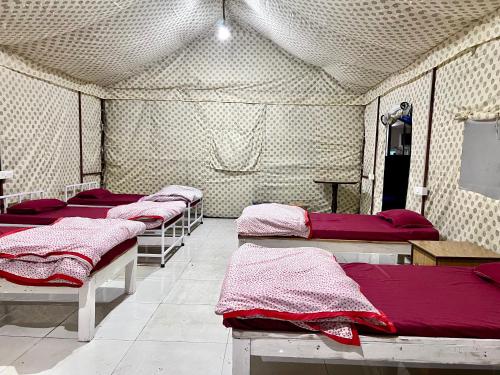 a row of beds in a room with red sheets at Shiv Shakti Yogpeeth Cottages in Rishīkesh