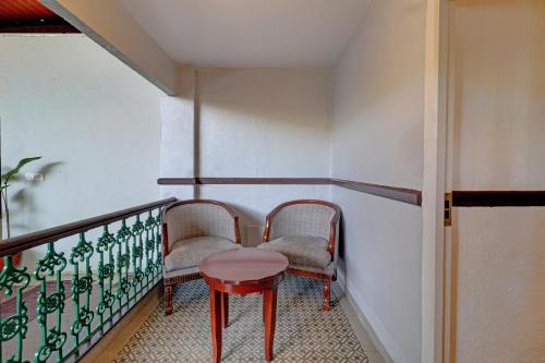 a balcony with two chairs and a red table at Citrus Chambers Mahabaleshwar in Mahabaleshwar