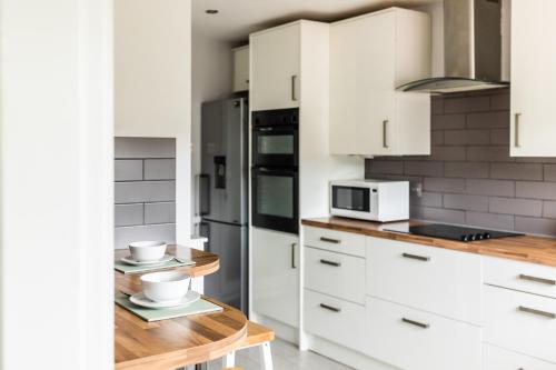 a kitchen with white cabinets and a wooden table at Lovely House in Welwyn with Garden and Off road parking in Welwyn Garden City