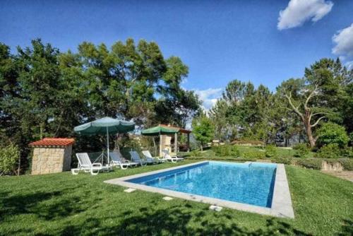 einen Pool in einem Garten mit Stühlen und einem Sonnenschirm in der Unterkunft Casa da Boavista Camélias de Basto-Turismo Rural in Celorico de Basto
