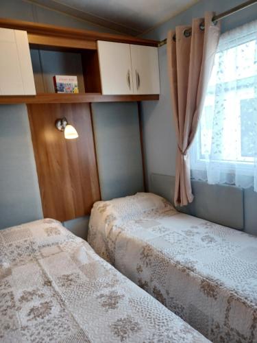 two beds in a small room with a window at Vista Caravan Hire in Seasalter