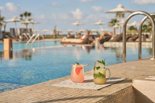 two cocktails sitting on a table next to a swimming pool at Nautilux Rethymno by Mage Hotels in Rethymno Town