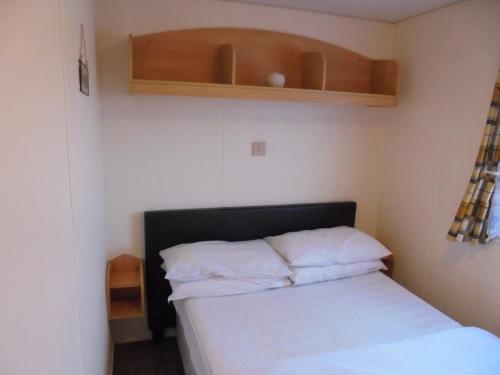 a small bedroom with a bed with white pillows at 6 berth 3 bedroom Northshore Skegness Emirates in Skegness