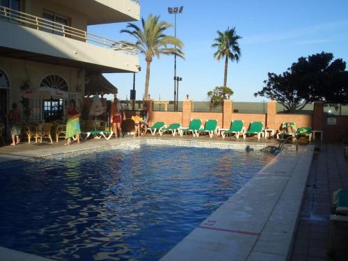 basen z zielonymi krzesłami i budynek w obiekcie Seafront apartment with open-air heated pool w mieście Fuengirola
