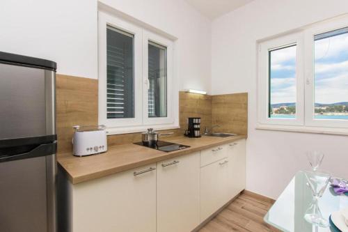 eine Küche mit weißen Schränken, einem Kühlschrank und Fenstern in der Unterkunft Riva 2 in Krapanj