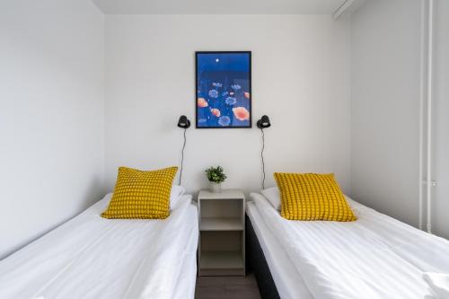 2 bedden in een kamer met witte muren en gele kussens bij Hiisi Homes Kirkkonummi Masala in Kirkkonummi