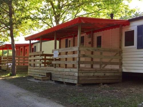 a wooden cabin with a red roof next to a house at Camping de Pujol - Chalets - Argeles sur Mer - Lotus - 6P in Argelès-sur-Mer