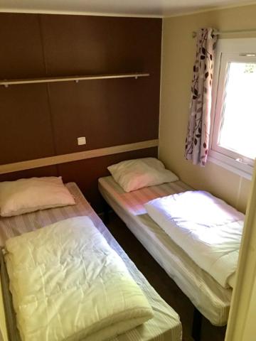 two beds in a small room with a window at Camping de Pujol - Chalets - Argeles sur Mer - Lotus - 6P in Argelès-sur-Mer