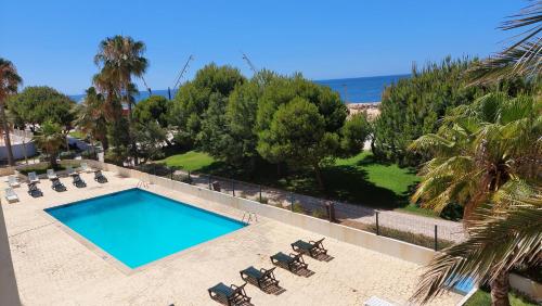 a swimming pool with chairs and the ocean in the background at Apartamento Kélyfos Beach by feriascomsol in Quarteira