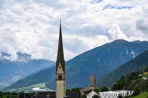 a church steeple in a town with mountains in the background at Apartement Noggler Zimmer mit Frühstück in Malles Venosta