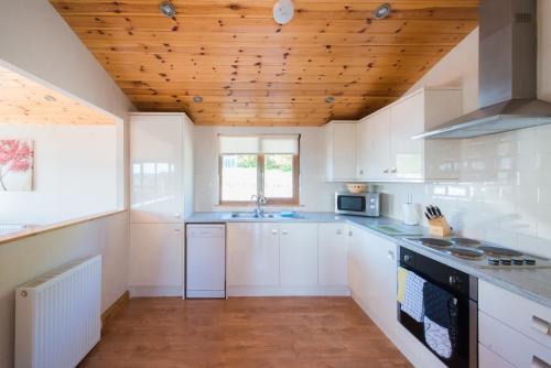 a kitchen with white cabinets and a wooden ceiling at Kingfisher Lodge with Hot Tub in Cupar