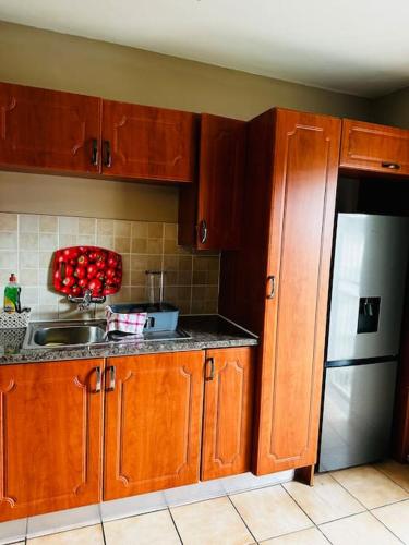 A Cozy Secure 2-Bed Apartment with a lovely garden في غابورون: مطبخ مع دواليب خشبية وثلاجة حديد قابلة للصدأ