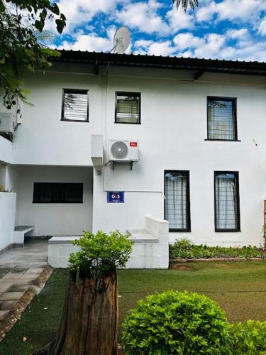 a white house with a tree stump in front of it at A Cozy Secure 2-Bed Apartment with a lovely garden in Gaborone