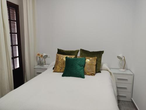 Un dormitorio con una cama blanca con almohadas verdes y doradas en Apartamentos BARBAS en Villanueva de los Castillejos