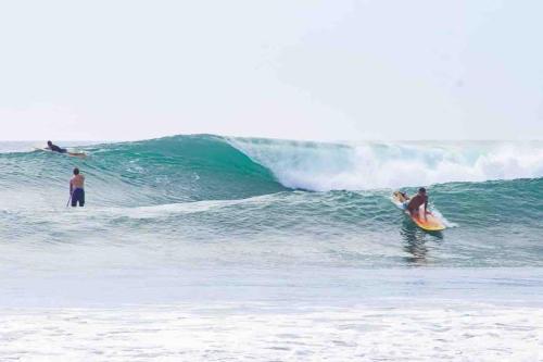 dos personas montando una ola en una tabla de surf en el océano en Casa Bus los Guanacastes, en Veintisiete de Abril