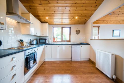 uma cozinha com armários brancos e um tecto de madeira em Skylark Lodge with Hot Tub em Cupar