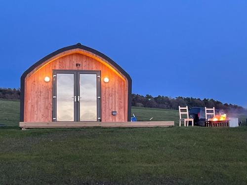 a wooden barn in a field with a grill at Hedgehog's Nest in Bathgate