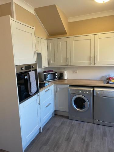 a kitchen with white cabinets and a washer and dryer at Sea Haven Northumberland in Seahouses